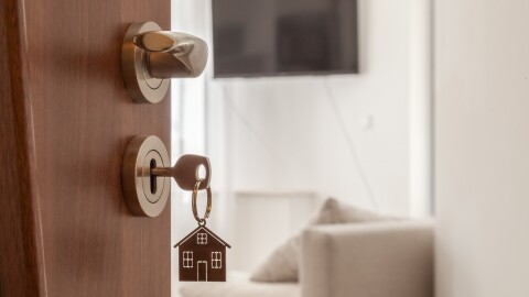 Open door to a new home. Door handle with key and home shaped keychain.