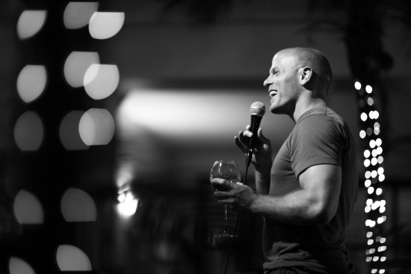 Tim Ferriss speaking at an event, smiling and holding a glass of wine.