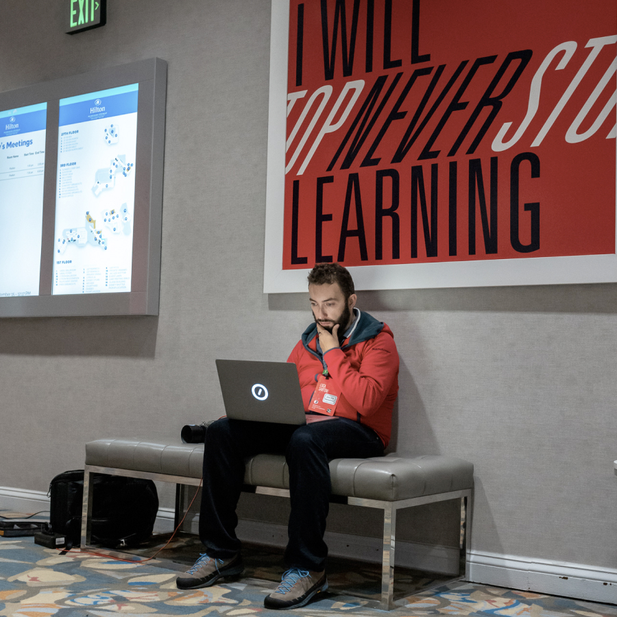 Automattician working on a laptop in front of a large sign that reads I will never stop learning