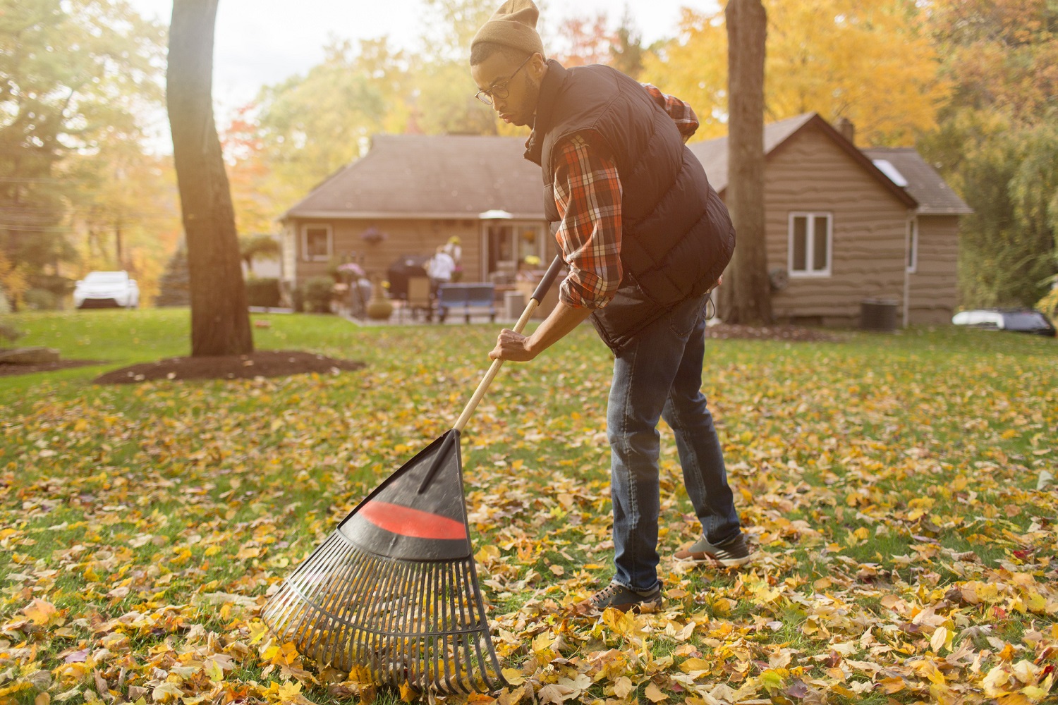 A young man raking leaves in his backyard in autumn