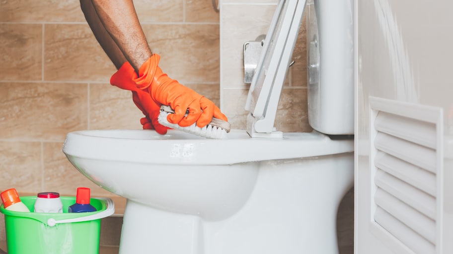 Detail of a man’s hand in gloves cleaning a toilet