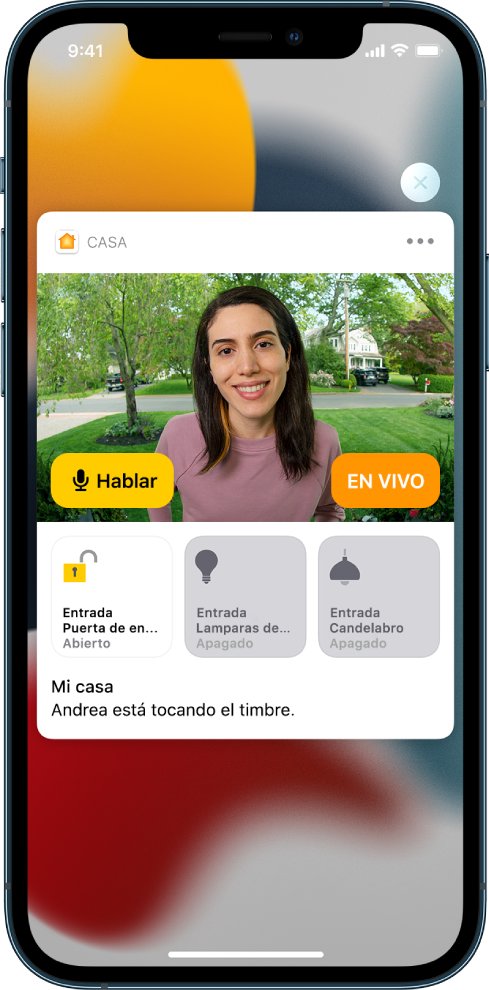Se muestra una notificación de Casa en la pantalla del iPhone. Muestra la foto de una persona en la puerta principal con el botón Hablar a la izquierda. En la parte inferior hay botones de accesorios de las luces de la puerta principal y la entrada. Las palabras “Ashley está tocando”. El botón Cerrar aparece en la parte superior derecha de la notificación.