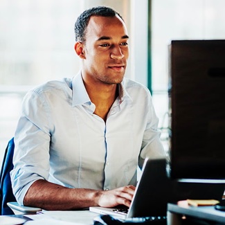 Man smiling sitting at a desk typing on a laptop