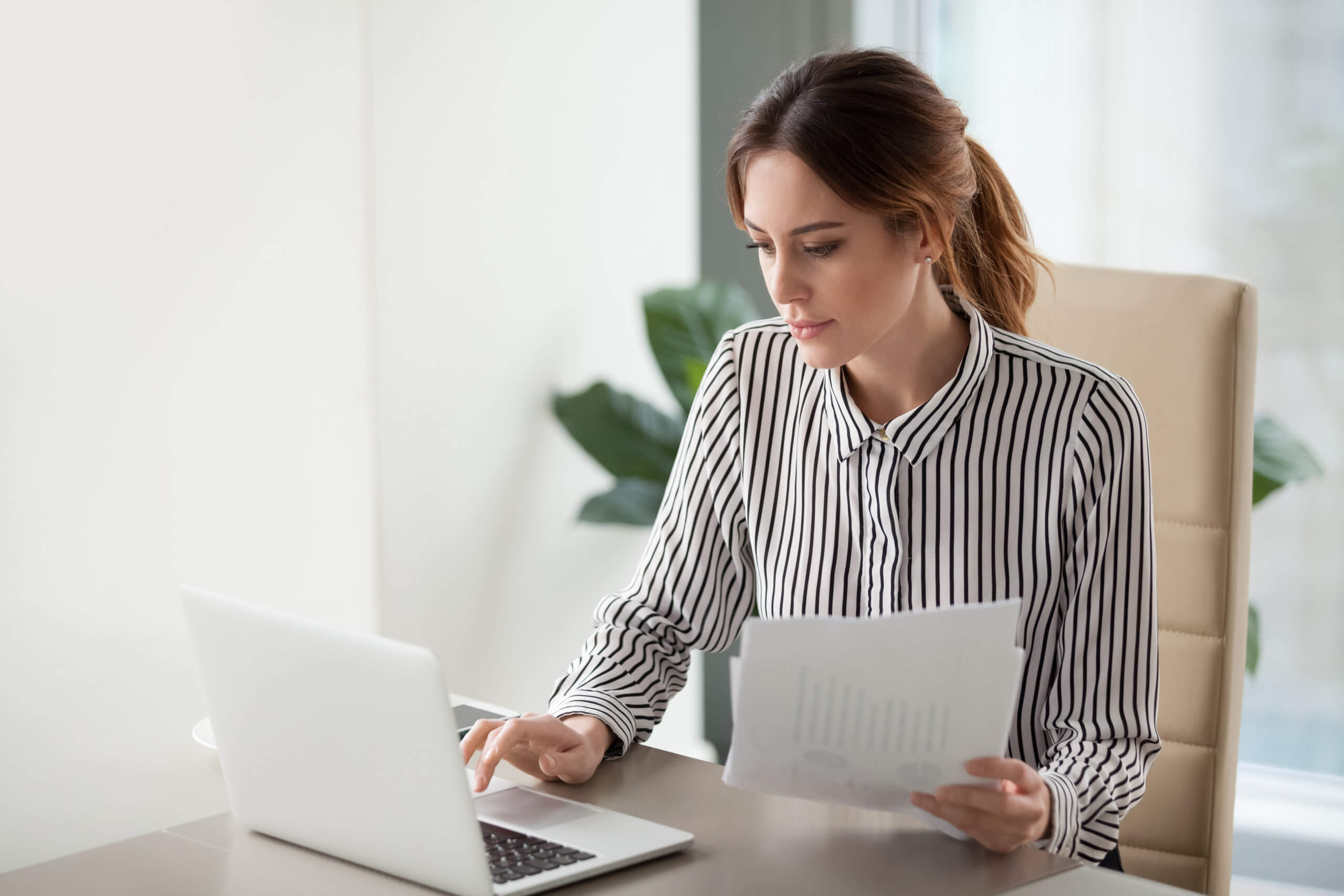 Serious focused businesswoman typing on laptop holding papers preparing report. Alternative to Quickbooks concept.