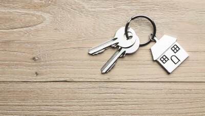 A set of metal keys with a home-shaped key ring sits on a wood table.