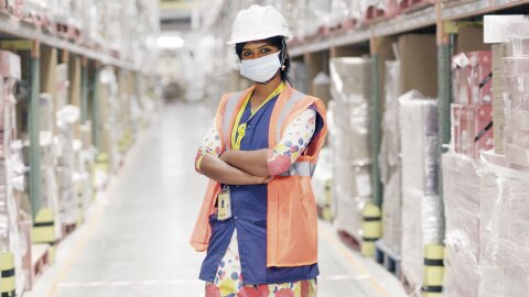 Amazon associate Sathya wears a high visibility vest, a face mask, and a hard hat standing in an Amazon sort center
