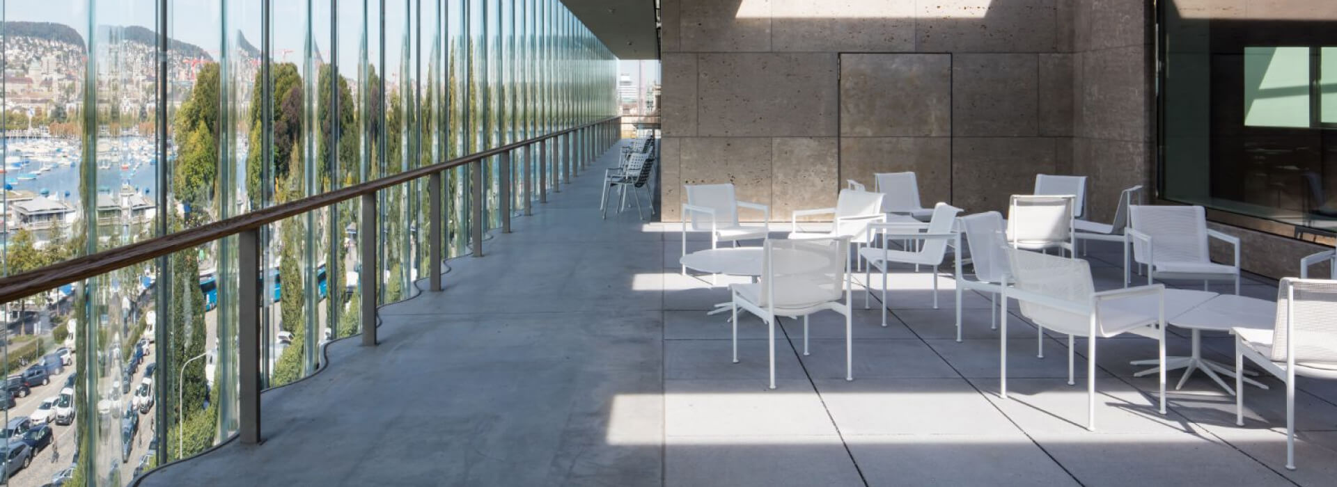 The patio of a modern office building, overlooking a city by a lake.