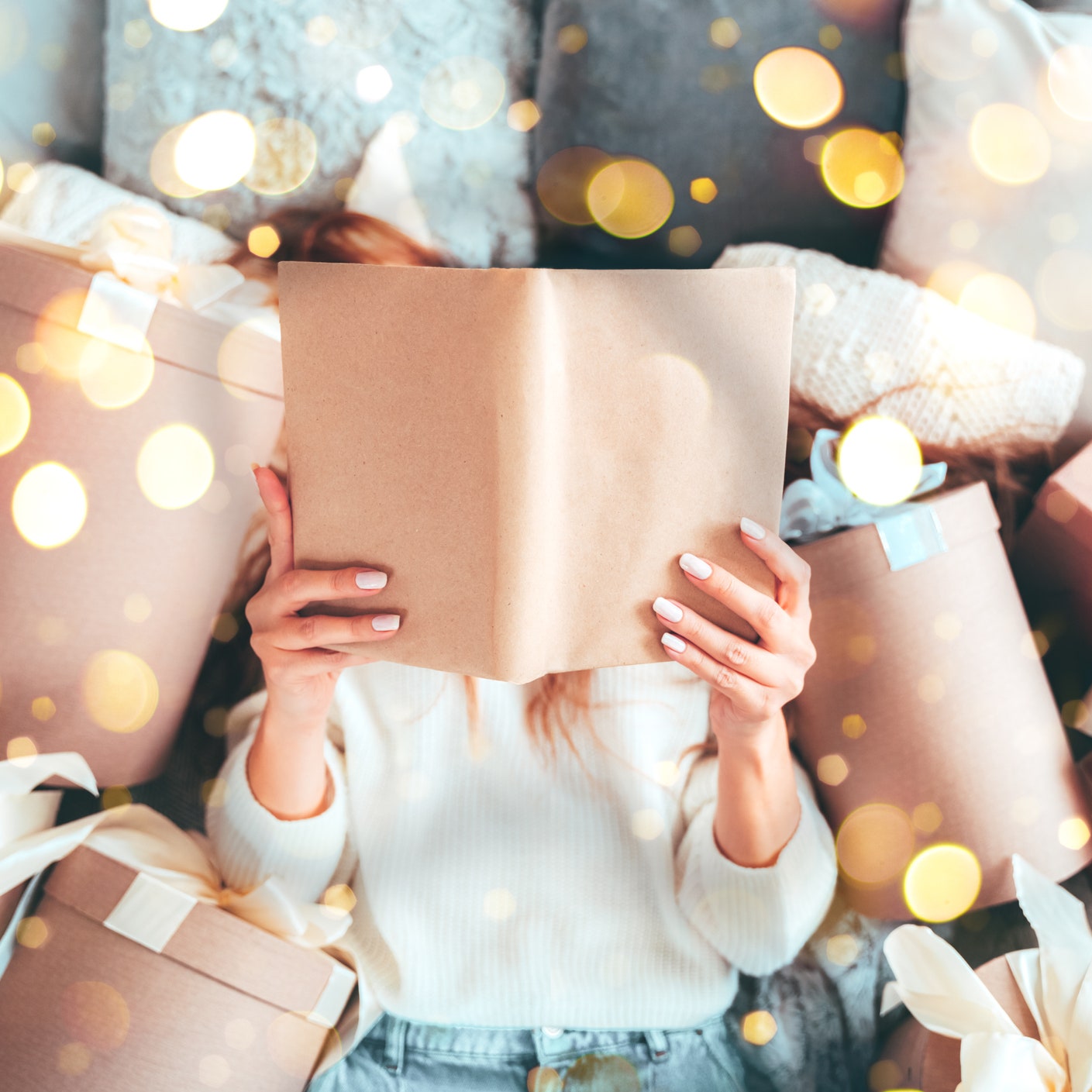 Woman is reading a book on a bed lying in between the gift boxes. She is a bookworm enjoying the Christmas and New Year...