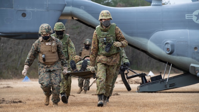 U.S. and Japanese soldiers carry a patient filled stretcher away from a landed helicopter.