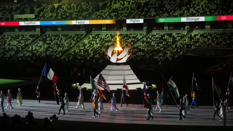 The Olympic flame burns as athletes and volunteers carry flags during the closing ceremony in...