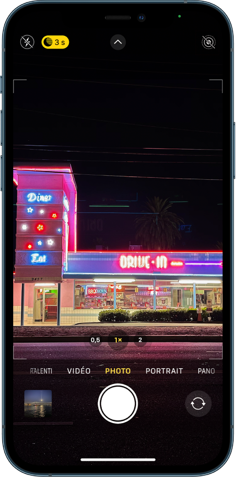 Écran de l’appareil photo en mode Photo. Les boutons correspondant au flash et au mode Nuit s’affichent dans l’angle supérieur gauche de l’écran. Le flash est désactivé et le mode Nuit est actif. Le bouton « Commandes de l’appareil photo » se trouve en haut au centre et le bouton « Live Photo » dans le coin supérieur droit. En bas de l’écran, de gauche à droite, se trouvent le bouton « Visualiseur de photos et vidéos », le bouton « Prendre une photo » et le bouton « Sélecteur de caméra - face arrière ».