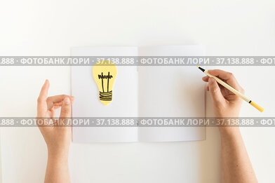 High angle view person s hand writing card with light bulb