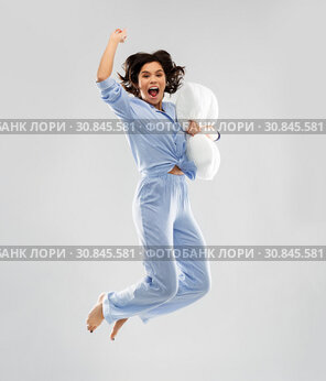 happy woman in blue pajama jumping with pillow