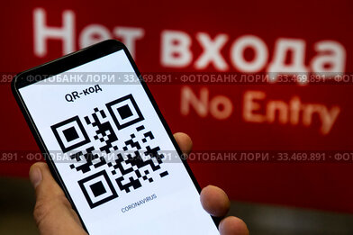 QR-код на телефоне с зашифрованной надписью "коронавирус" на фоне входа московское метро в городе Москве, Россия