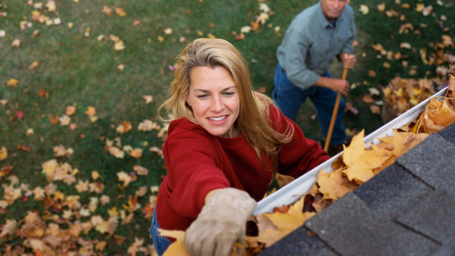 A couple cleaning the gutter from autumn leaves