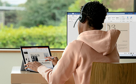 Young person using headsets working in front of the laptop and desktop computer.