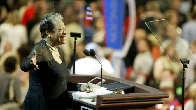 Maya Angelous stands at a podium, addressing a large crowd blurred behind her. 