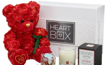 A teddy bear covered in hearts with a candle and box of gummies.