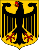 Coat of arms featuring a large black eagle with wings spread and beak open. The eagle is black, with red talons and beak, and is over a gold background.