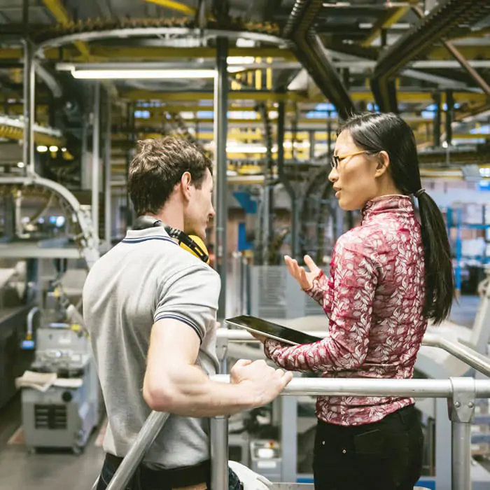 Woman holding tablet in discussion with man in industrial setting