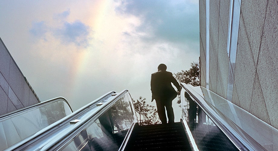 Man going toward rainbow at top of subway escalator