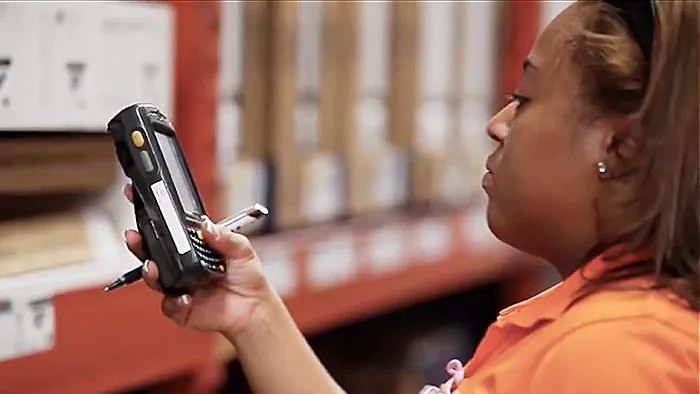 Worker reading screen of handheld scanning device in store aisle