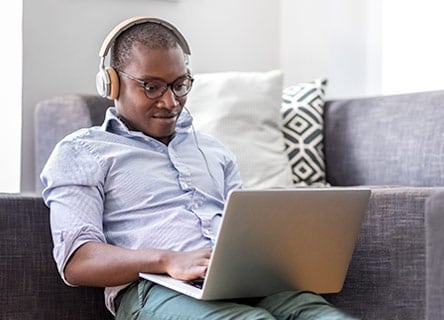 Homem de óculos e fones de ouvido trabalhando no laptop em home office.