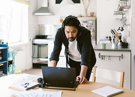 Homem de cabelos escuros e fones de ouvido trabalhando em home office em seu laptop.