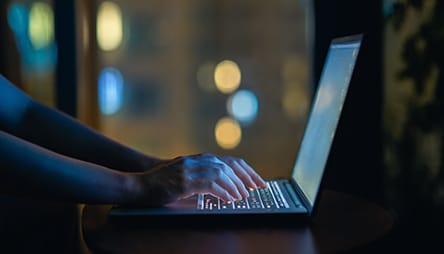 A woman typing on a laptop at night