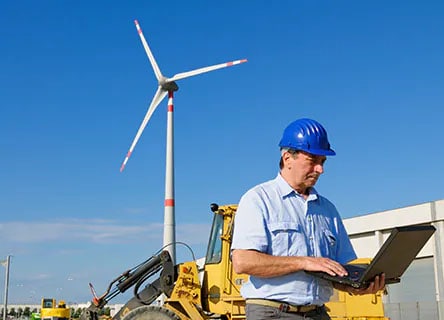 man with computer in front of wind turbine
