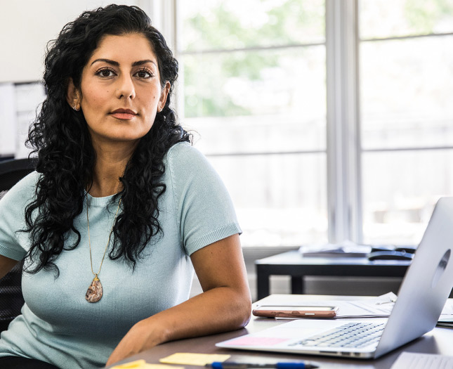 Young woman looking at the camera and working on a desk with a laptop