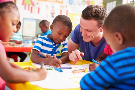 Volunteer teacher helping a class of preschool kids drawing.