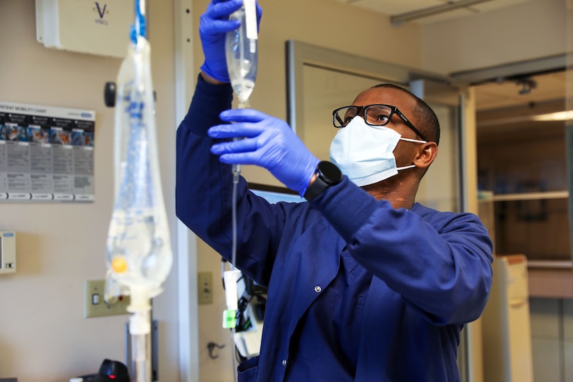 A sailor wearing a face mask gives a patient a new IV bag.