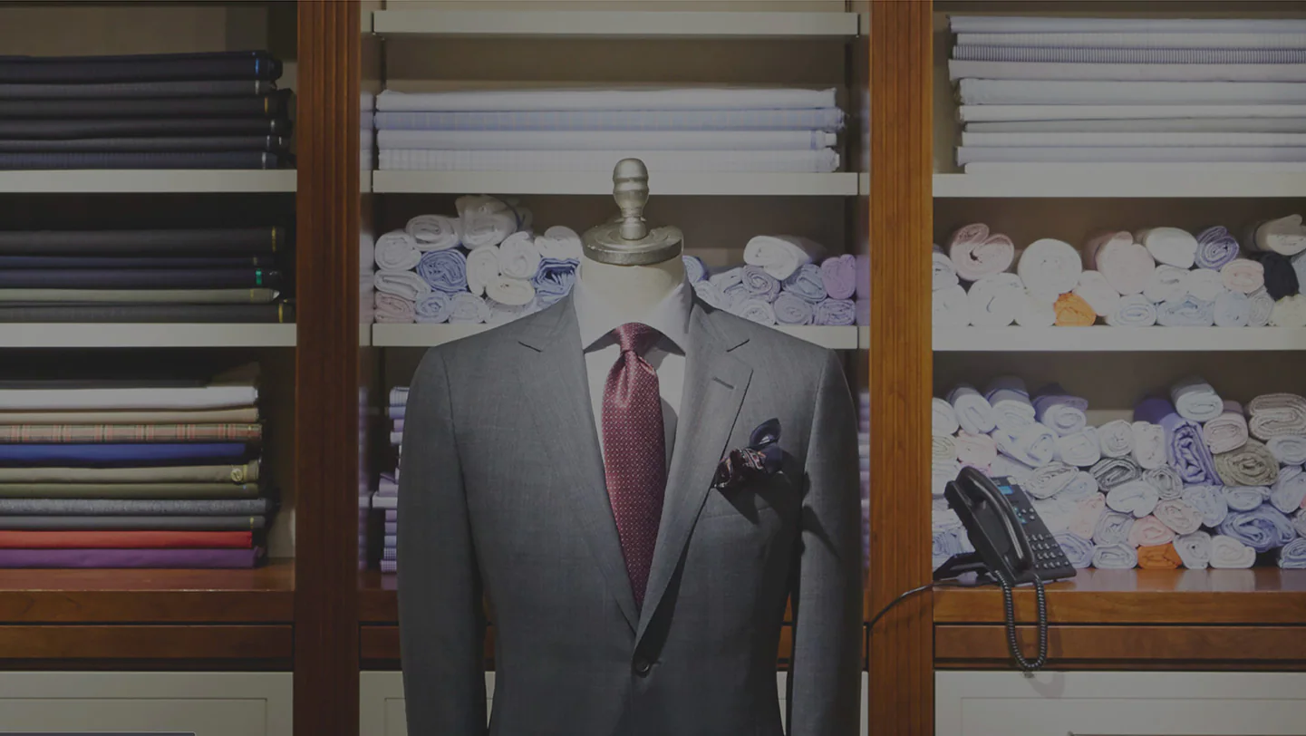 Mannequin wearing suit with stacks and rolls of fabric on shelves behind it