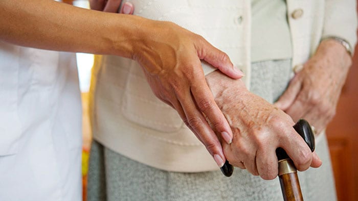 An aid's hand guides an elderly hand holding a cane