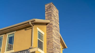 a brick chimney along a yellow house with blue sky in background