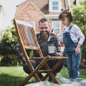 Father and daughter painting chair outside