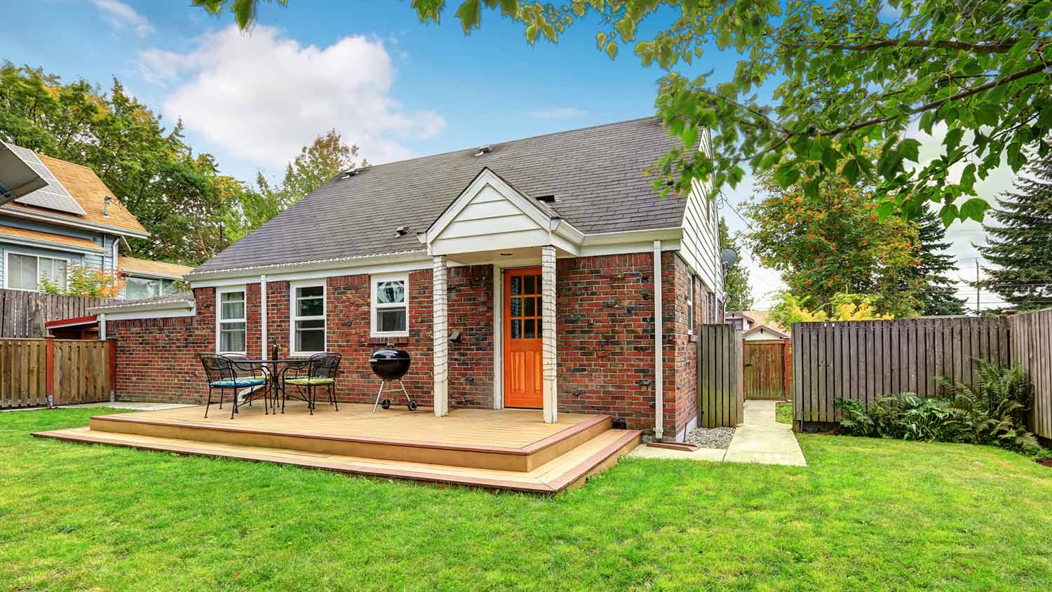 Wood deck off brick house of fenced in yard