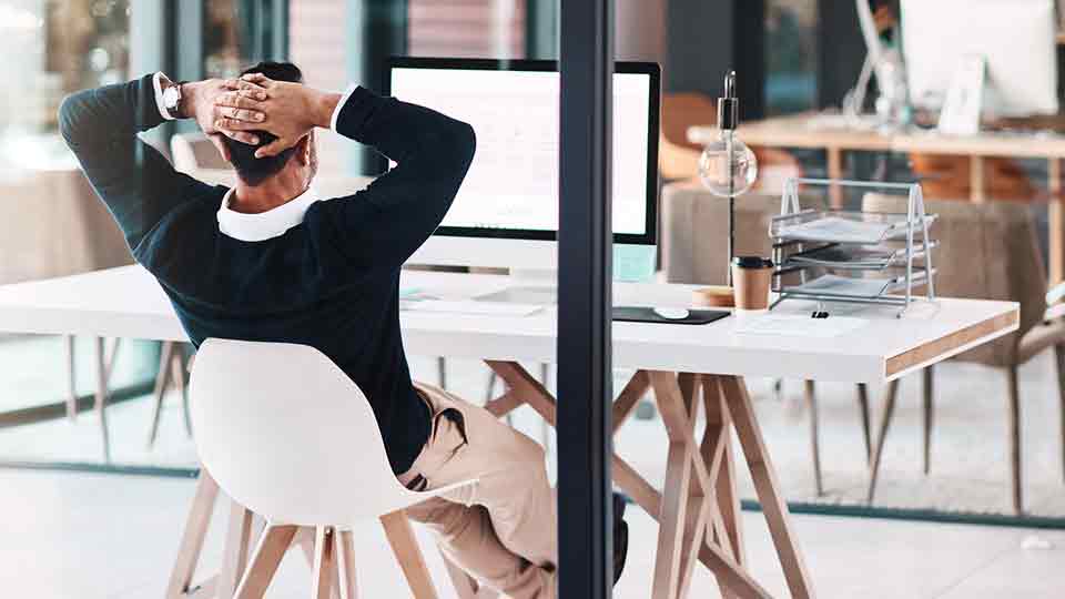 A professional leans back in a chair, and looks into a computer monitor