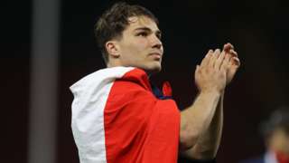 Antoine Dupont applauds with a France flag round his shoulders