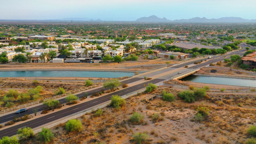 Scottsdale, Arizona highway over a river with buildings, green trees, and mountains in the distance