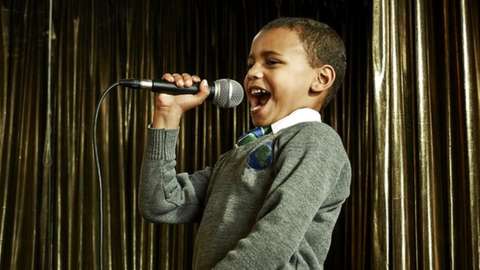 A young boy in his school uniform singing into a microphone
