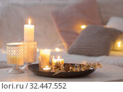 Christmas decoration with burning candles on white table against the background of sofa with plaids and pillows. Cozy home and holiday concept. Стоковое фото, фотограф Майя Крученкова / Фотобанк Лори