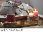 Red cup of tea on tray with burning candles on background sofa with pillows. Cozy home concept. Стоковое фото, фотограф Майя Крученкова / Фотобанк Лори