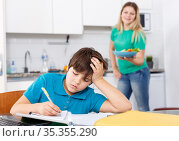 Boy doing homework, mother cooking. Стоковое фото, фотограф Яков Филимонов / Фотобанк Лори