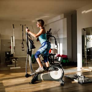 Woman in workout clothes working on on an elliptical machine with a wood floor, mirror and other workout equipment