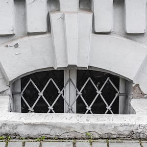 basement window with wire bars sits behind stone square egress with decorative stone details above window