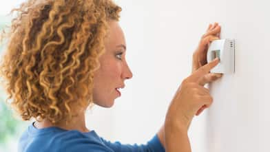 A woman setting the temperature via a thermostat