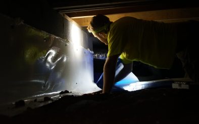 Crew with headlamp installing vapor barrier in crawl space
