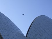 Top of an unrecognizable curvy building under blue sky with a helicopter so far in the distance that it resembles a sparrow